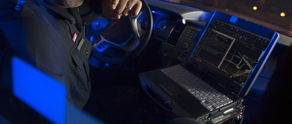 A police officer using a rugged laptop while sitting in the driver's seat of his car