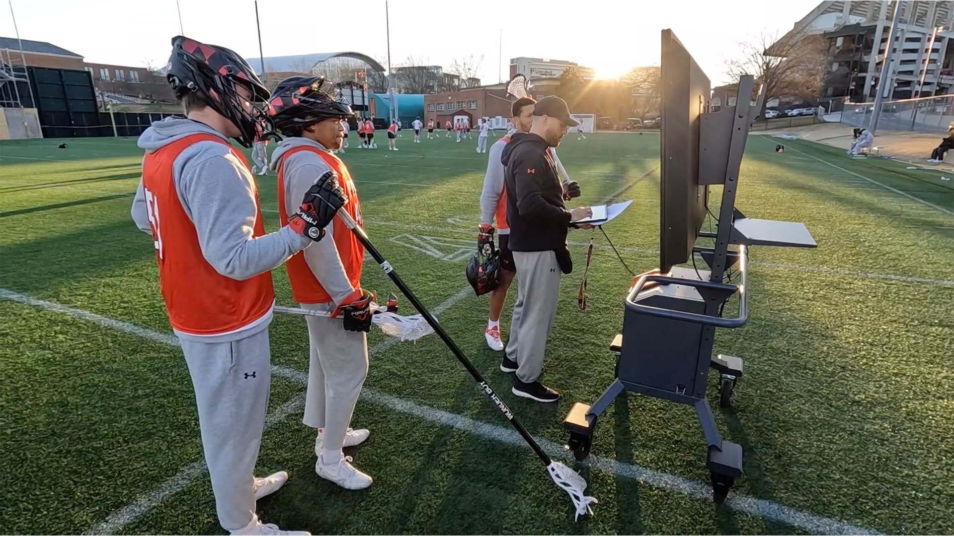 small group of athletes and coaches at a grass practice field standing in front of a Bretford Cordless Explorer Display Cart